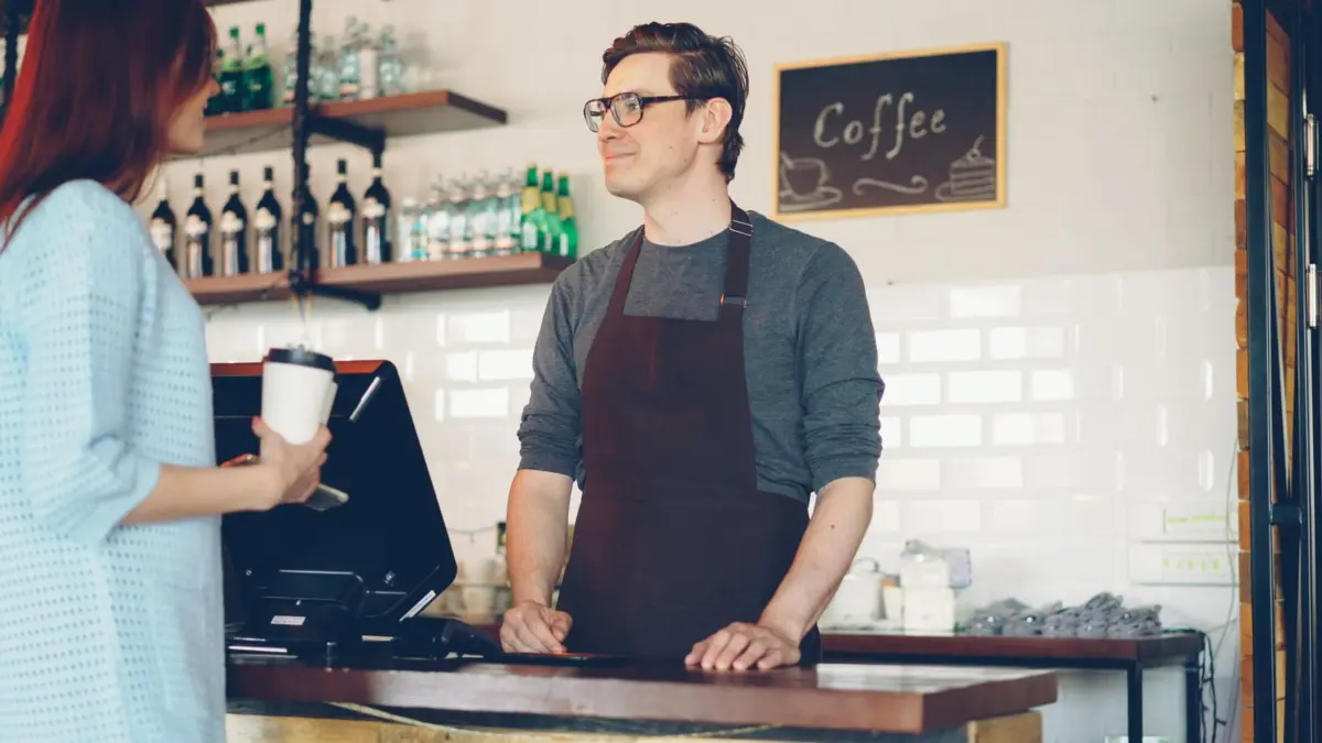 Cafe owner in an apron talking to a customer at the counter to sort out a complaint