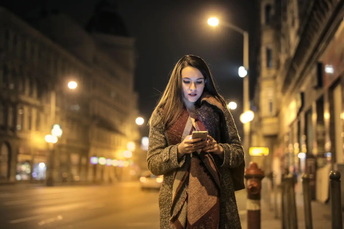 Woman walking down a city street at night checking a business on her smartphone