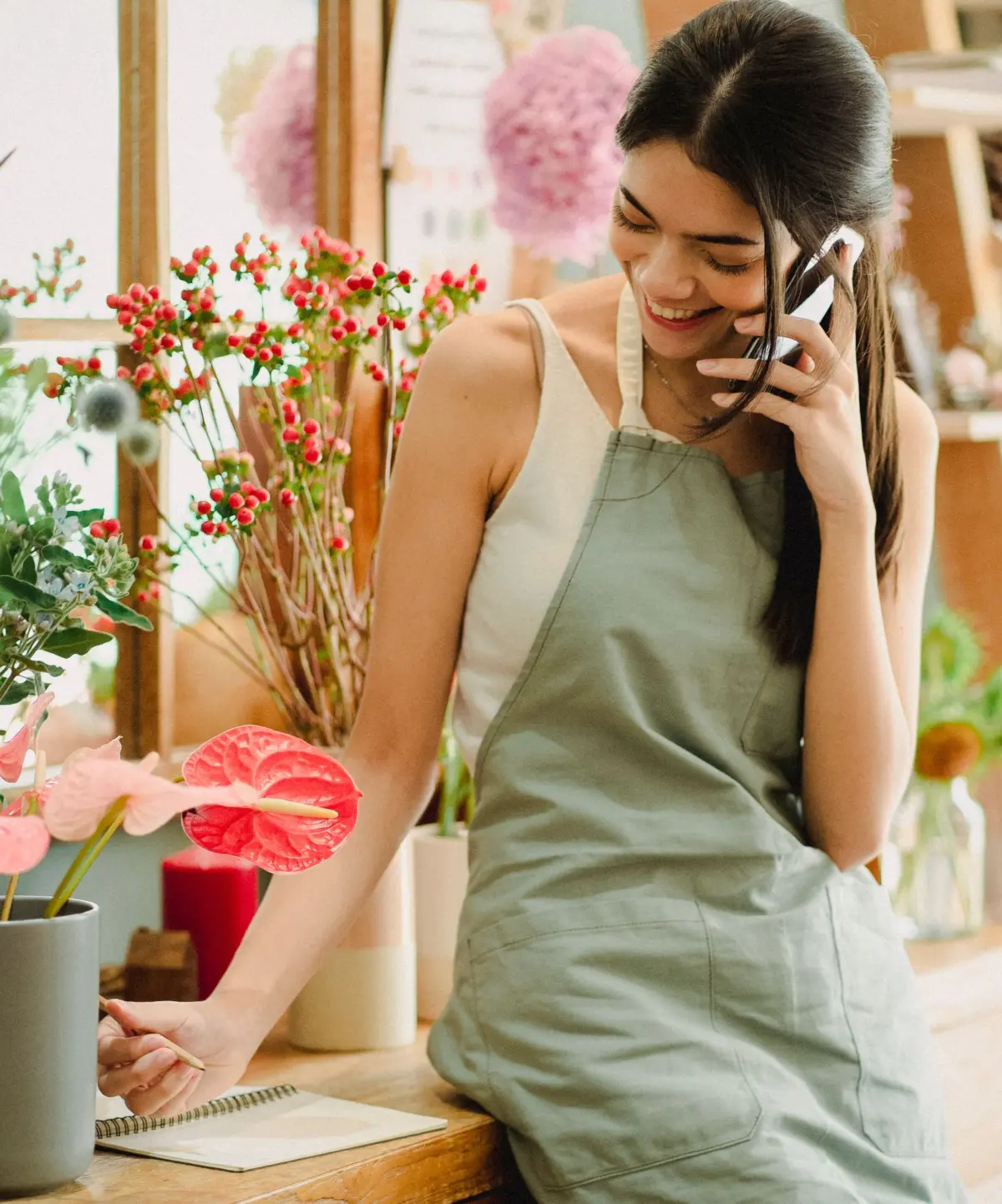 Smiling florist taking a customer order by phone in her busy flower shop