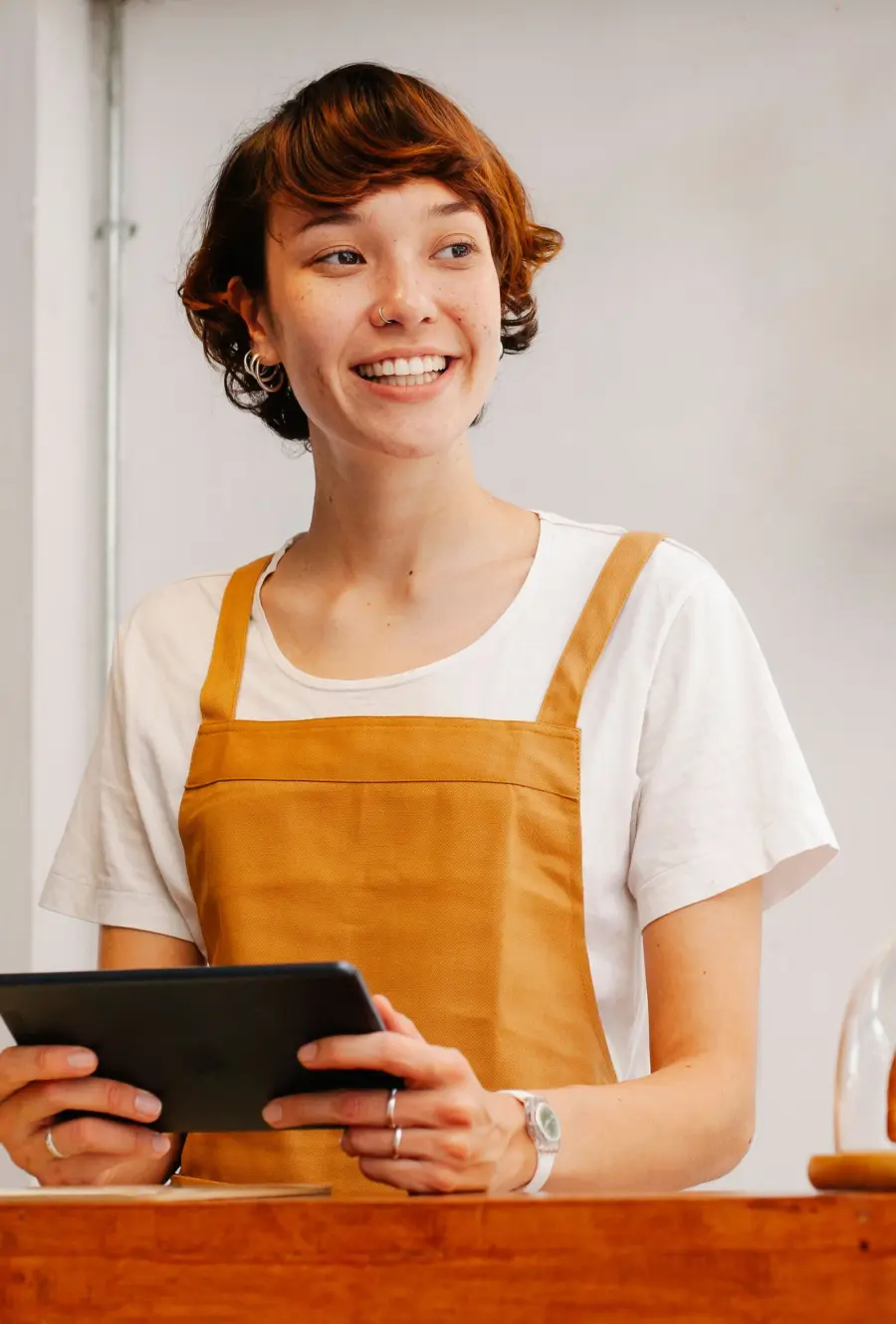 Smiling cafe owner holding a tablet at the counter, checking her local search presence