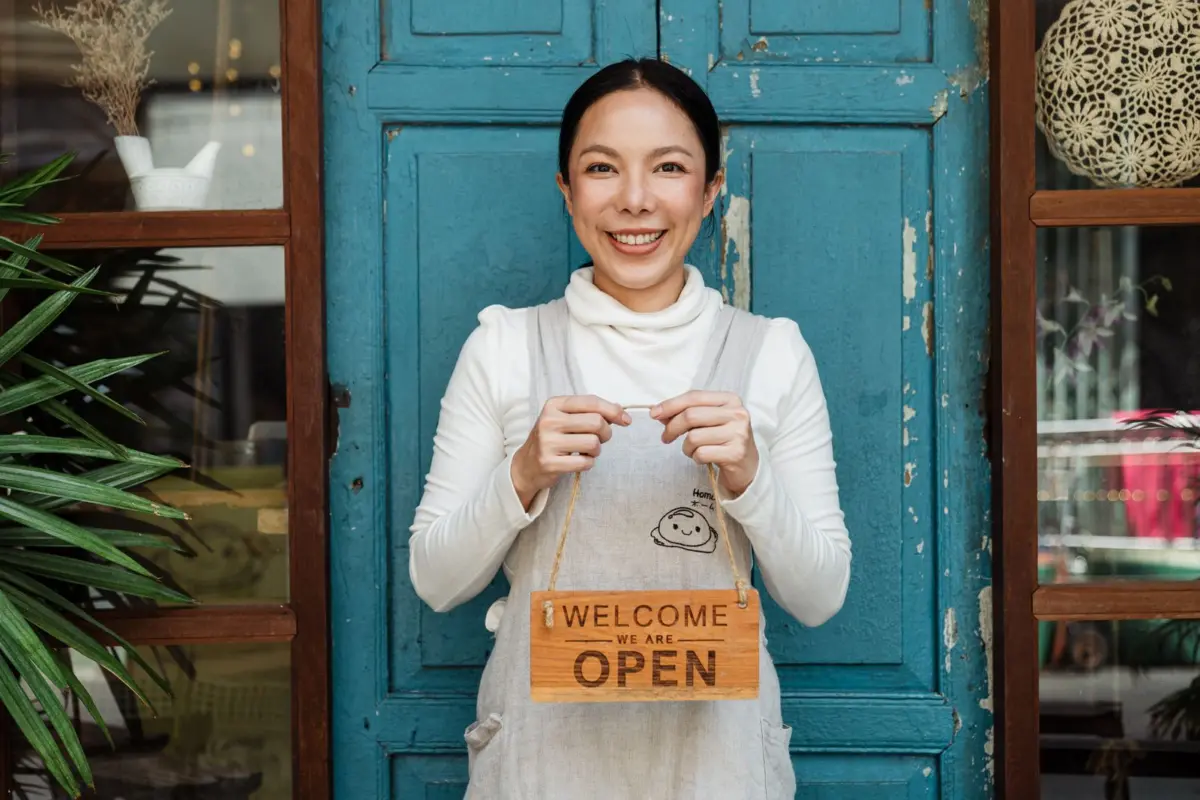 New café owner smiling at the door holding a welcome we are open sign