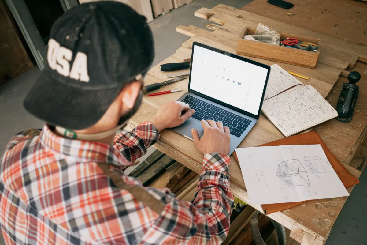 Carpenter in his workshop reporting a fake review on his laptop with phone in hand