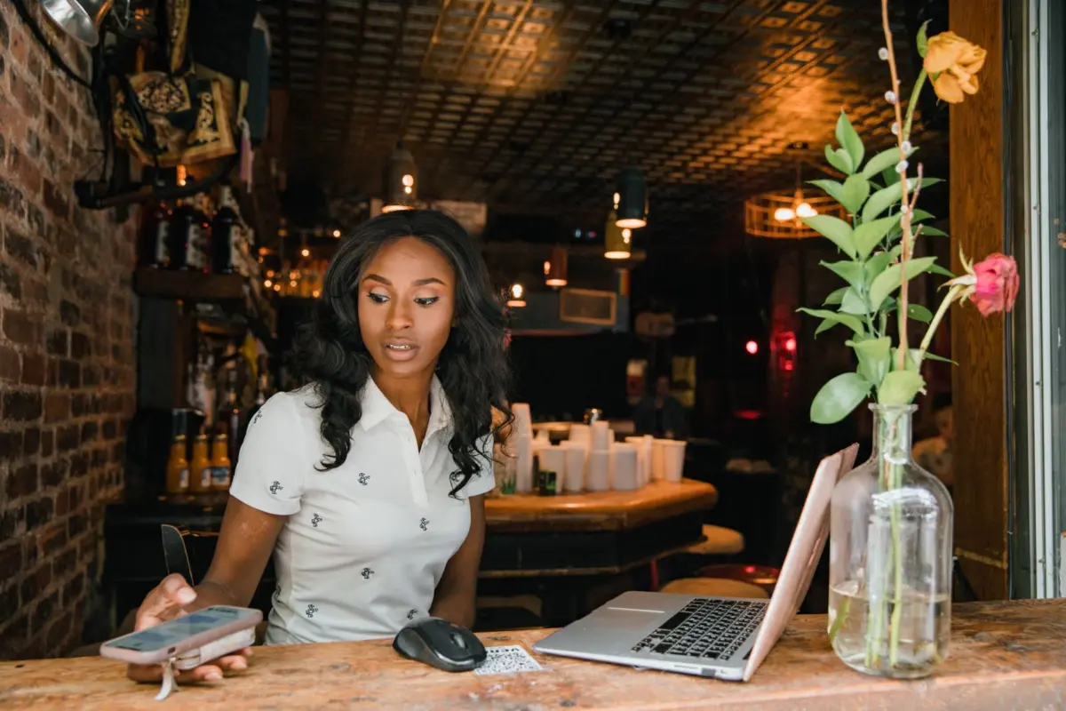 Café owner using a laptop and phone at the counter to update her website